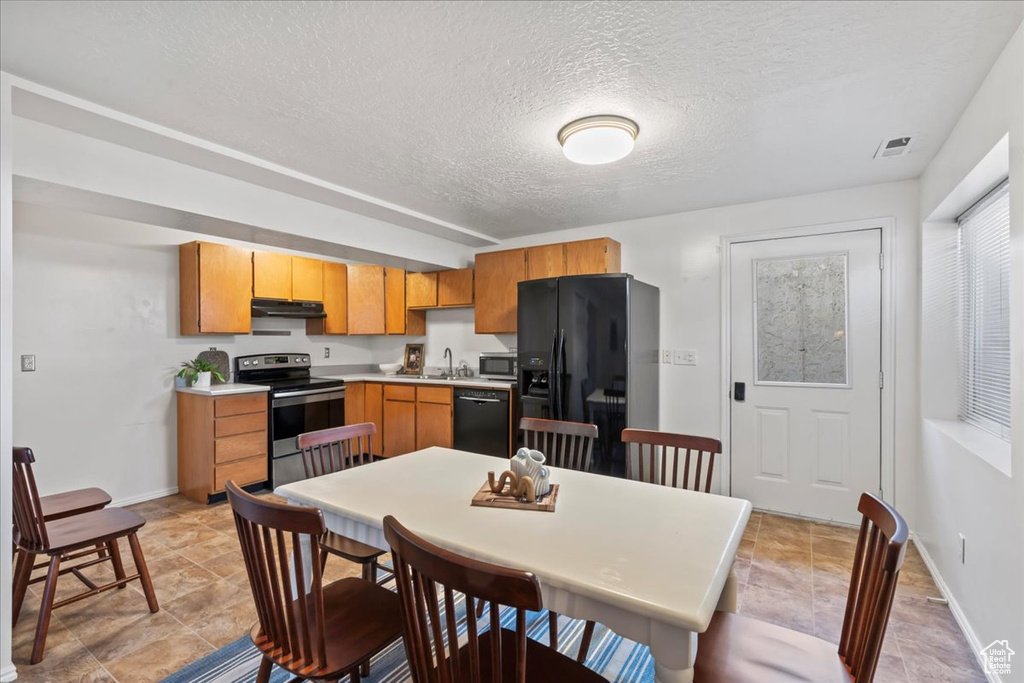 Kitchen with black appliances, under cabinet range hood, light countertops, a textured ceiling, and baseboards