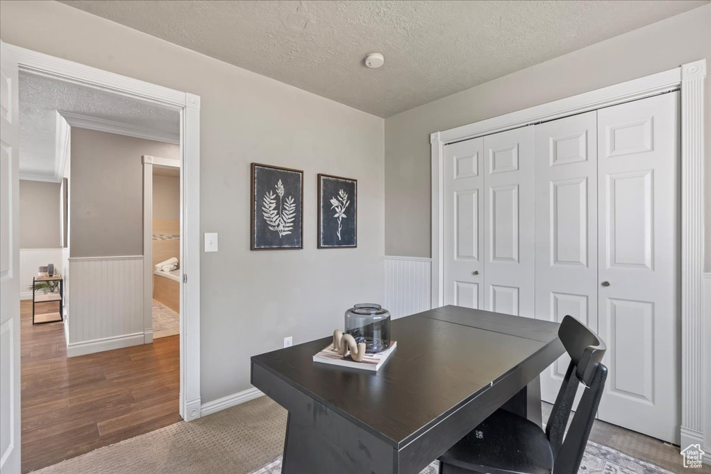 Office featuring a wainscoted wall, a textured ceiling, wood finished floors, and baseboards