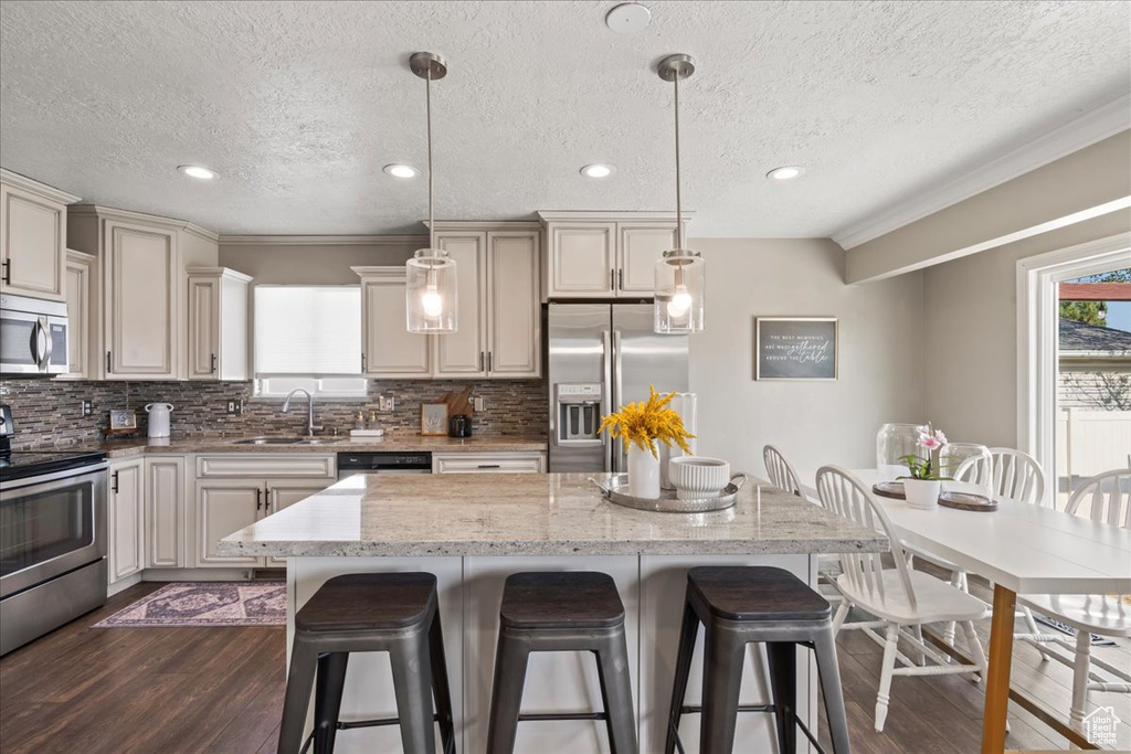 Kitchen featuring appliances with stainless steel finishes, a sink, a kitchen bar, dark wood-style flooring, and a textured ceiling