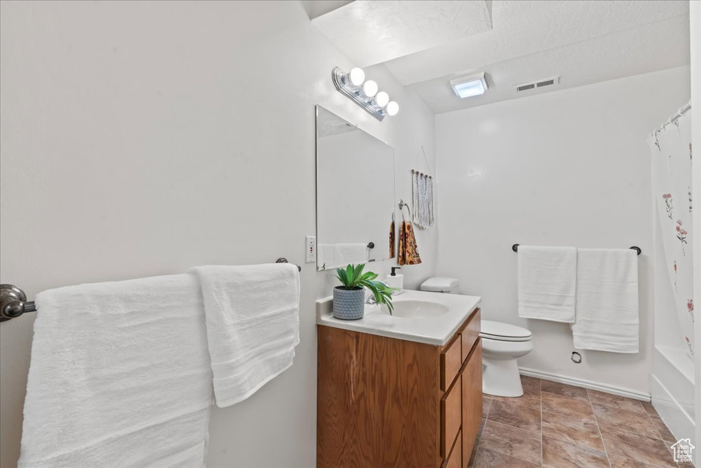 Bathroom with vanity, toilet, baseboards, shower / tub combo, and stone finish floors