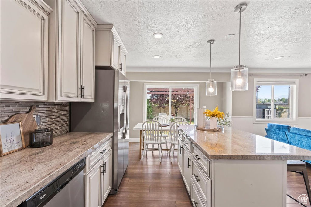 Kitchen featuring dishwasher, a textured ceiling, dark wood finished floors, a center island, and light stone counters