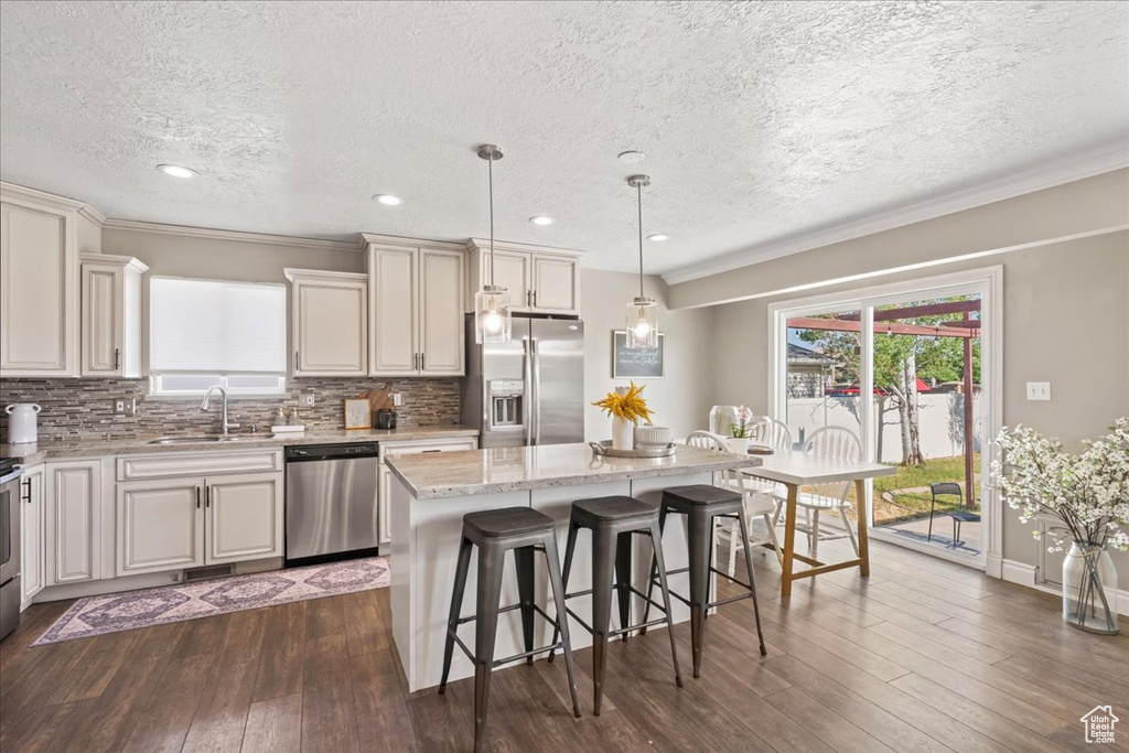 Kitchen featuring appliances with stainless steel finishes, a sink, a breakfast bar area, a textured ceiling, and a kitchen island