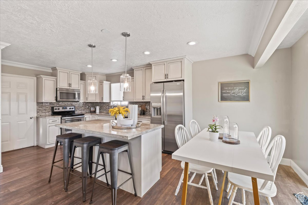 Kitchen featuring appliances with stainless steel finishes, a center island, dark wood finished floors, a kitchen breakfast bar, and decorative backsplash
