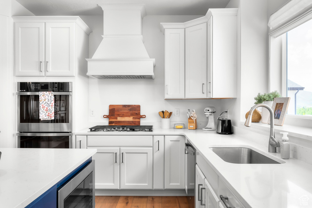 Kitchen with appliances with stainless steel finishes, premium range hood, wine cooler, light countertops, and white cabinets