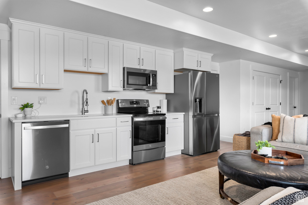 Kitchen featuring stainless steel appliances, light countertops, dark wood-style flooring, white cabinetry, and recessed lighting