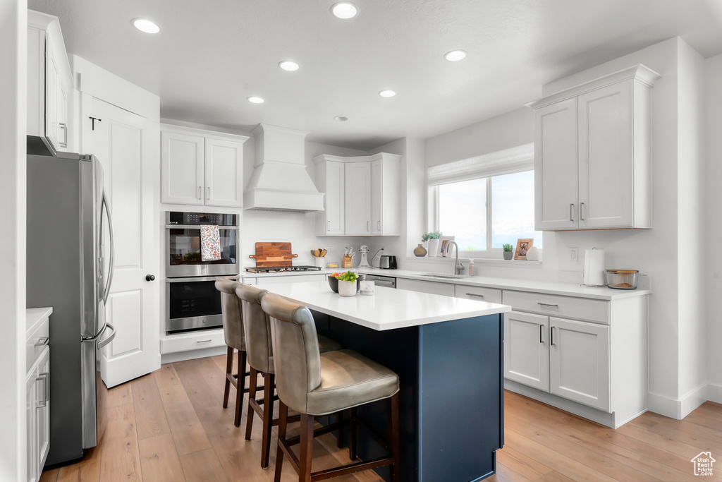Kitchen featuring stainless steel appliances, custom range hood, a breakfast bar, recessed lighting, and white cabinets