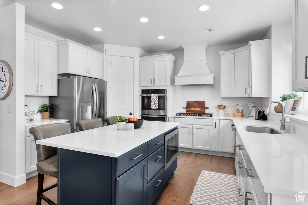 Kitchen featuring blue cabinets, stainless steel appliances, white cabinetry, a kitchen bar, and light wood-style floors