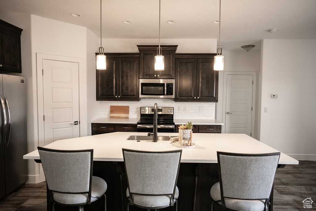 Kitchen featuring appliances with stainless steel finishes, backsplash, a center island with sink, light countertops, and recessed lighting