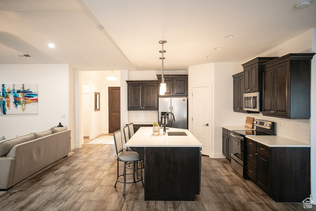 Kitchen featuring appliances with stainless steel finishes, open floor plan, backsplash, dark wood-style floors, and light countertops