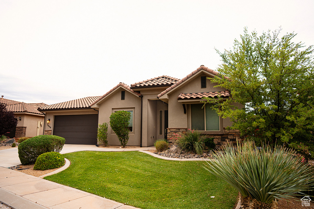 Mediterranean / spanish house with stucco siding, stone siding, a front lawn, a tiled roof, and driveway