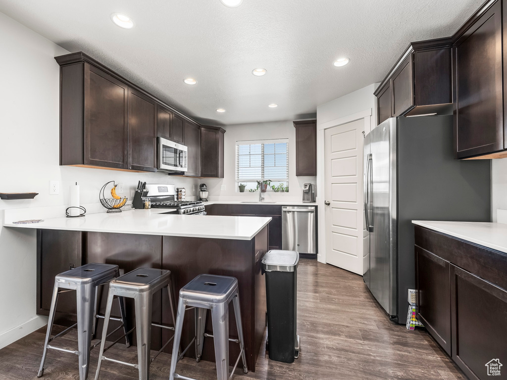 Kitchen with appliances with stainless steel finishes, dark brown cabinets, a peninsula, a kitchen breakfast bar, and light countertops