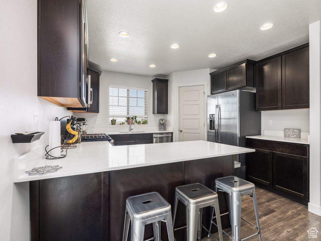 Kitchen featuring appliances with stainless steel finishes, a peninsula, dark wood-style floors, light countertops, and a breakfast bar area