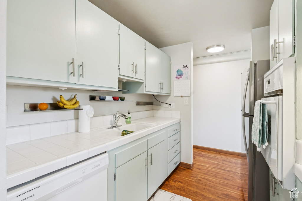 Kitchen featuring white dishwasher, light wood-style flooring, tile counters, white cabinetry, and freestanding refrigerator
