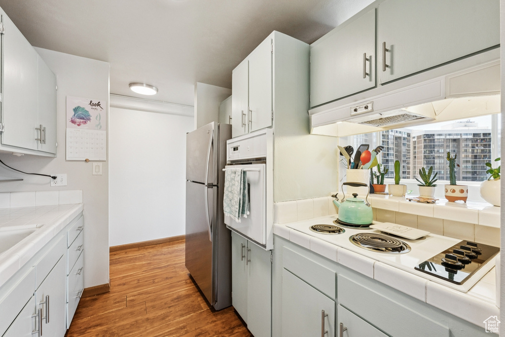 Kitchen featuring white appliances, tile counters, wood finished floors, and white cabinets
