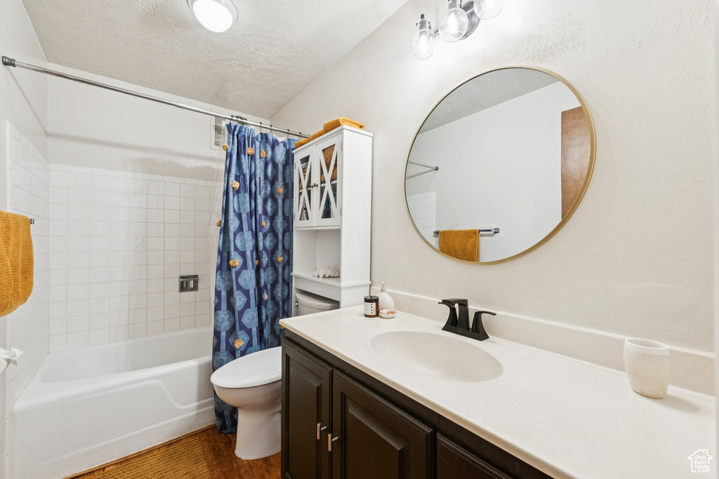 Full bath featuring vanity, shower / tub combo with curtain, wood finished floors, and a textured ceiling