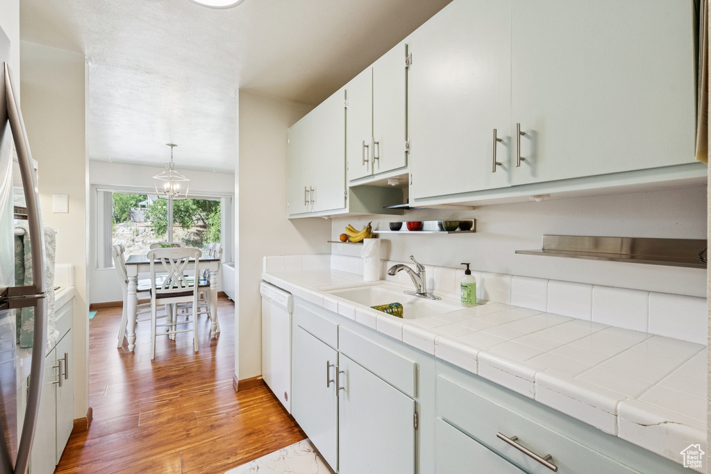Kitchen featuring white dishwasher, stainless steel refrigerator, light wood finished floors, white cabinetry, and hanging light fixtures