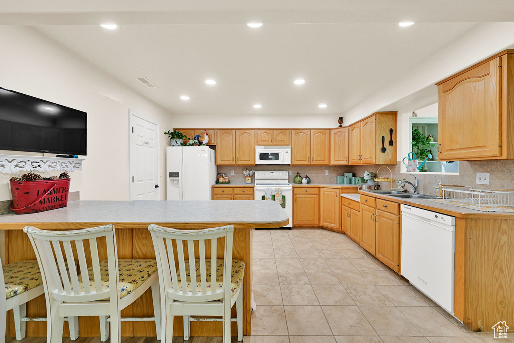 Kitchen featuring white appliances, light countertops, a breakfast bar, tasteful backsplash, and a peninsula