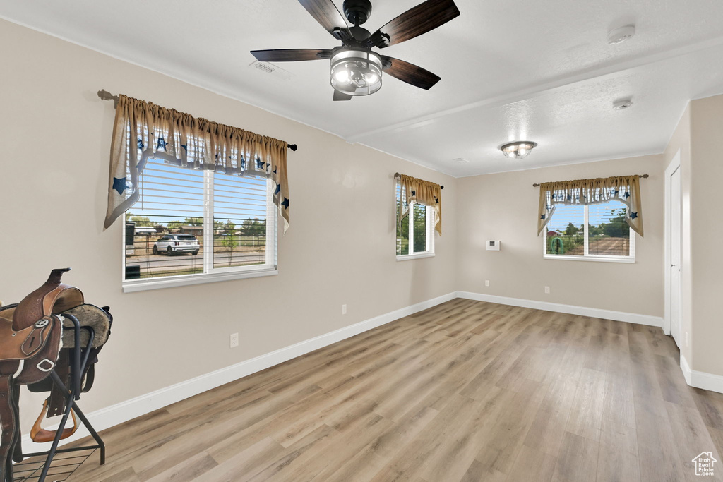 Empty room with light wood-style flooring, ceiling fan, and a smoke detector