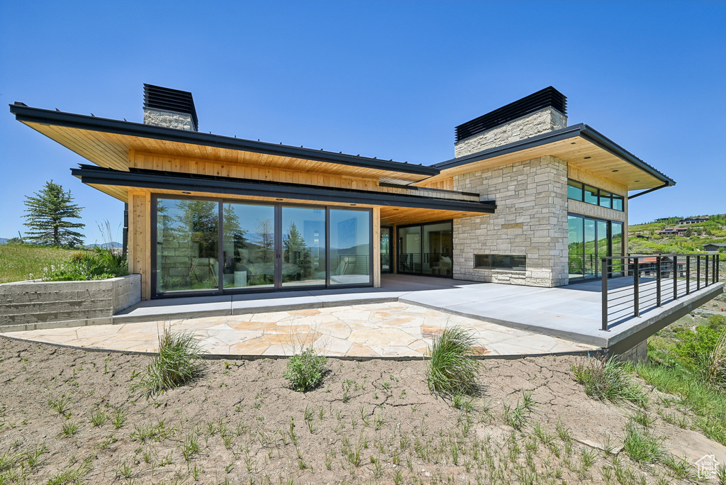 Rear view of house featuring a chimney, stone siding, and a patio area