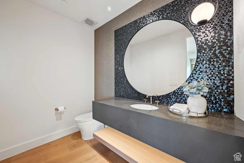 Bathroom with toilet, wood finished floors, decorative backsplash, vanity, and baseboards
