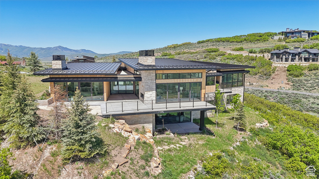 Rear view of house with a standing seam roof, metal roof, a chimney, stone siding, and a mountain view