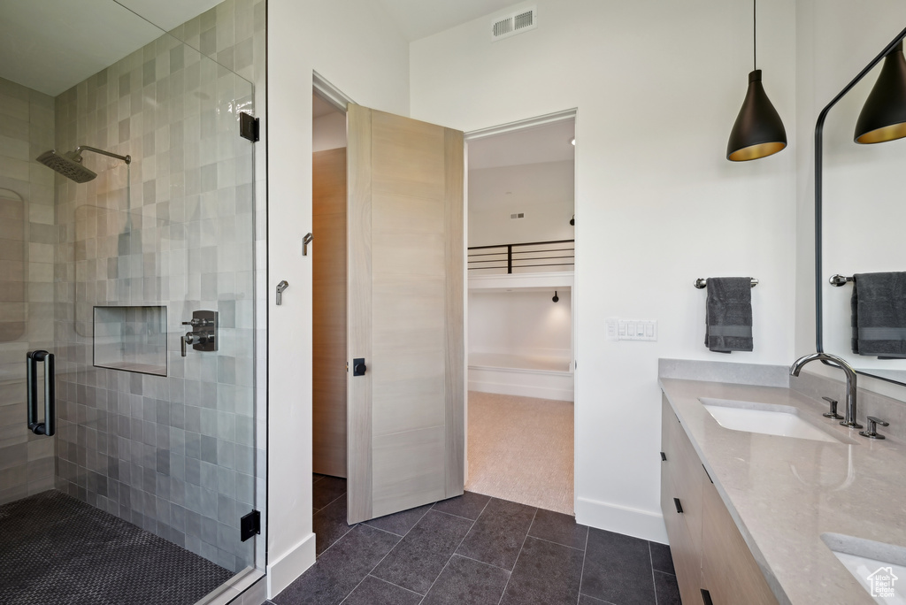 Bathroom featuring a shower stall, double vanity, tile patterned floors, and baseboards