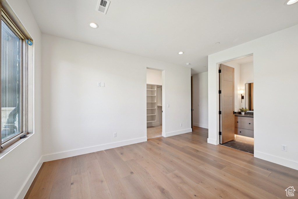 Unfurnished bedroom with light wood-type flooring, baseboards, a spacious closet, and recessed lighting