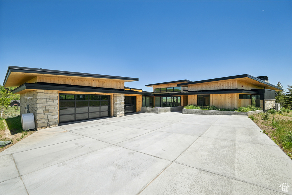 Contemporary house with stone siding, driveway, and a garage