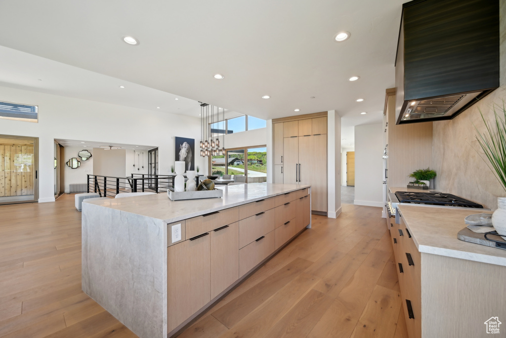 Kitchen featuring modern cabinets, wall chimney range hood, light brown cabinets, light wood-type flooring, and recessed lighting
