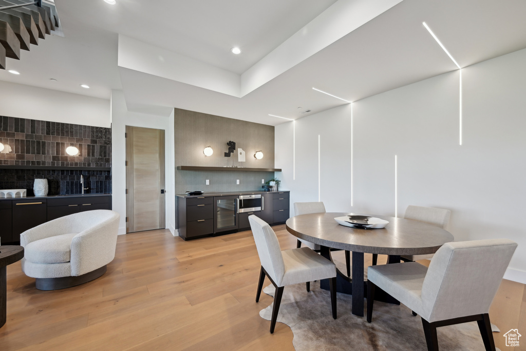 Dining space featuring wine cooler, bar with sink, light wood finished floors, and recessed lighting