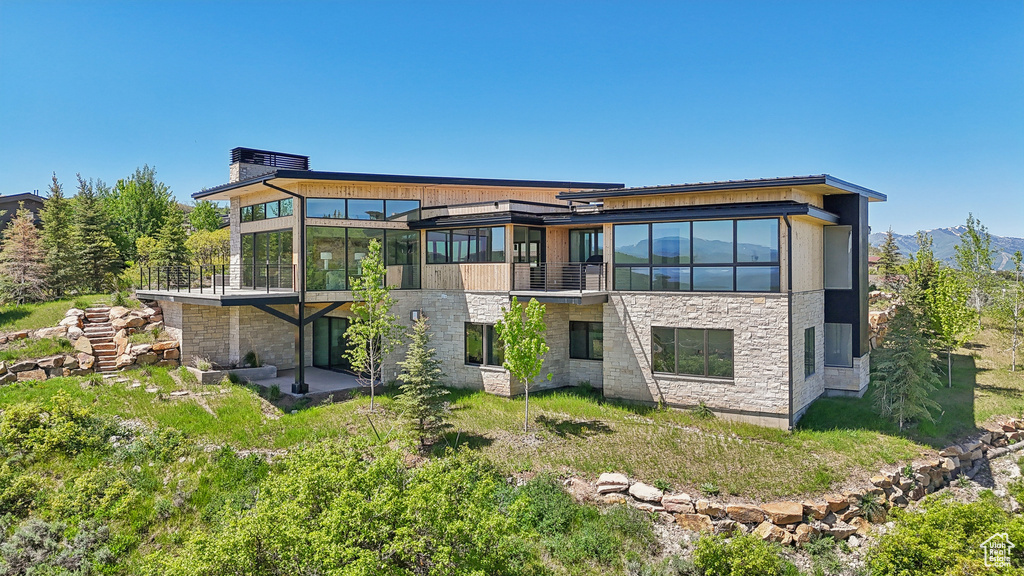 Rear view of house featuring a sunroom, stone siding, a balcony, and a mountain view