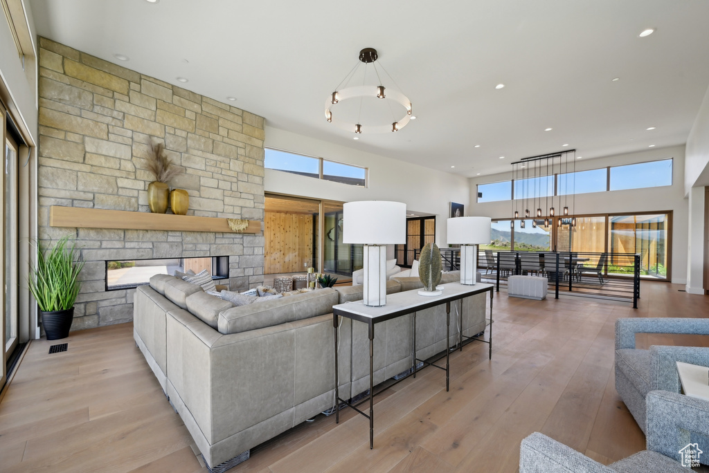 Living room with a stone fireplace, a towering ceiling, light wood-style flooring, and recessed lighting