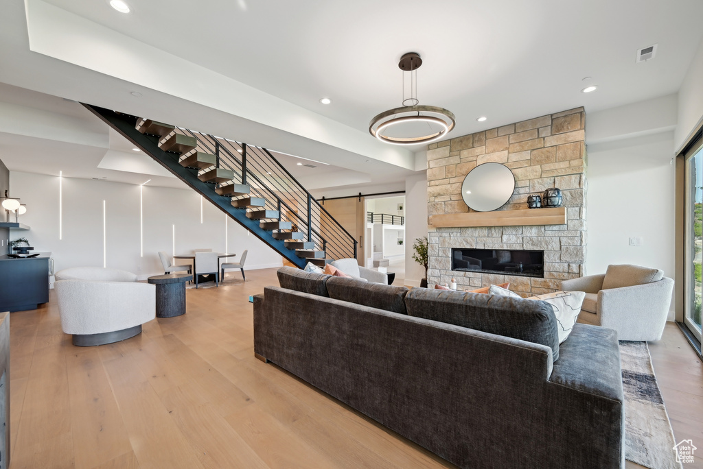Living area featuring a barn door, light wood finished floors, recessed lighting, stairs, and a stone fireplace