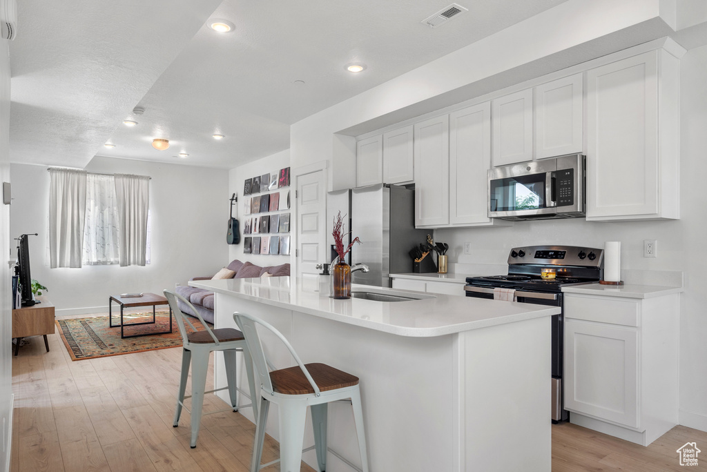 Kitchen with stainless steel appliances, light wood finished floors, open floor plan, a breakfast bar area, and recessed lighting