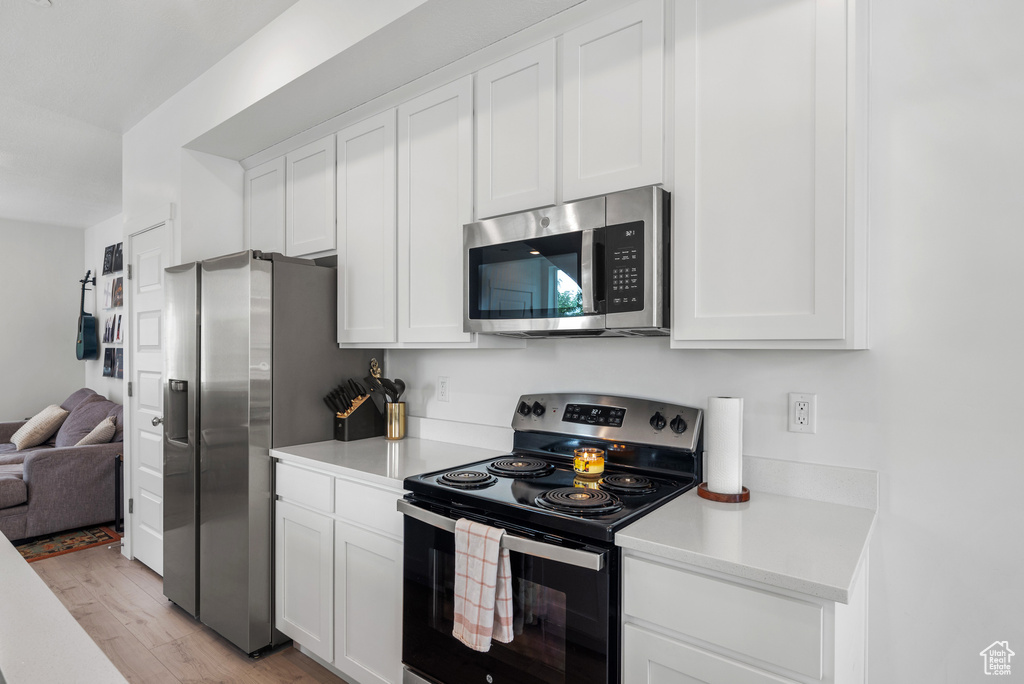 Kitchen with appliances with stainless steel finishes, light countertops, light wood-style floors, white cabinetry, and open floor plan