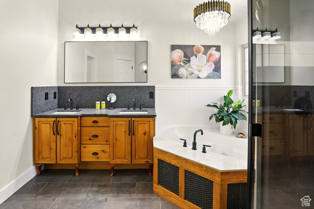 Bathroom with double vanity, a whirlpool tub, a wainscoted wall, a chandelier, and decorative backsplash