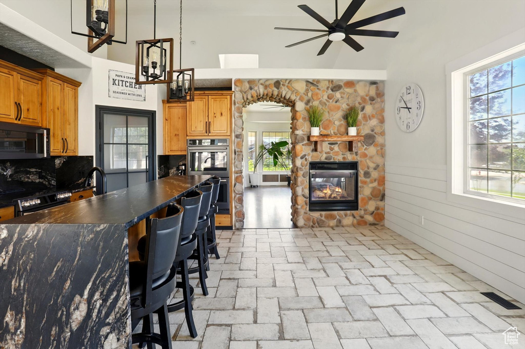Kitchen featuring black microwave, dark countertops, a ceiling fan, stainless steel double oven, and a stone fireplace