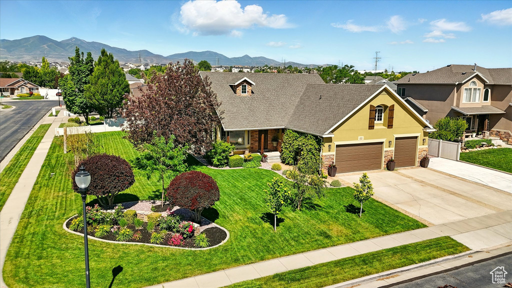 View of front of home with stone siding, driveway, a front lawn, a mountain view, and stucco siding
