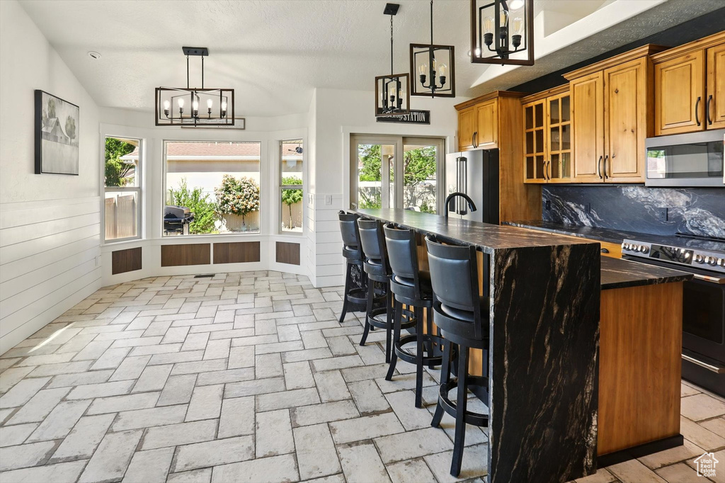 Kitchen with stainless steel appliances, a chandelier, a breakfast bar, glass insert cabinets, and brown cabinets