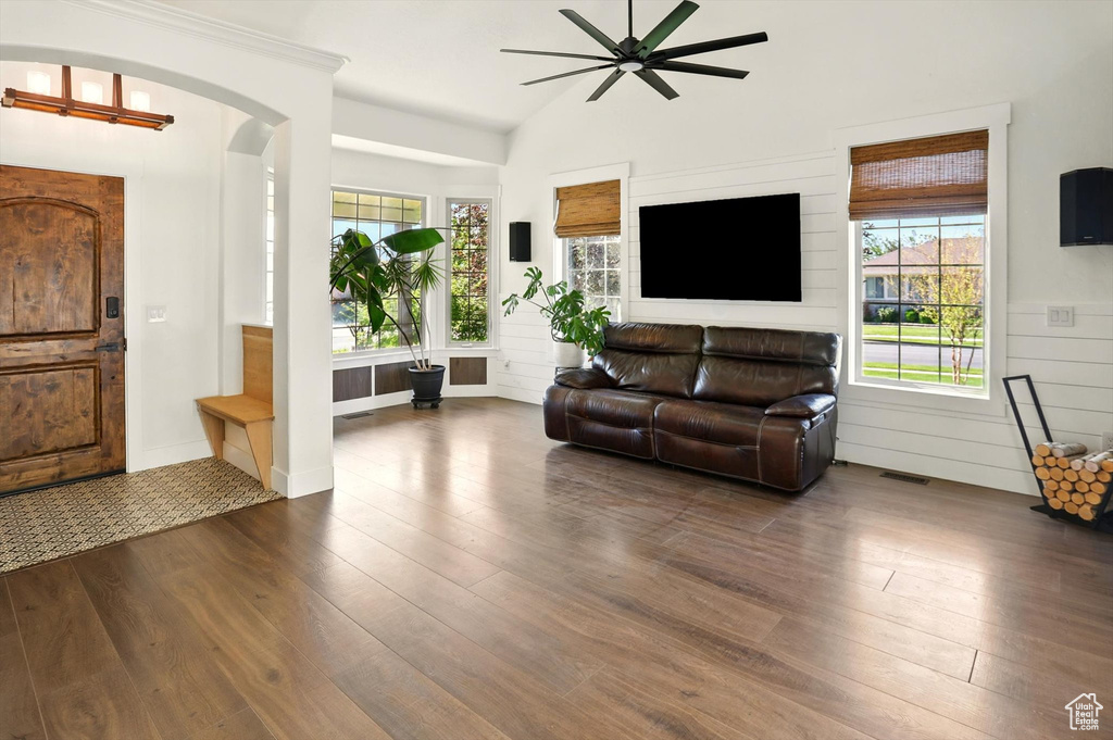 Living area featuring dark wood-style floors, ceiling fan, arched walkways, and lofted ceiling
