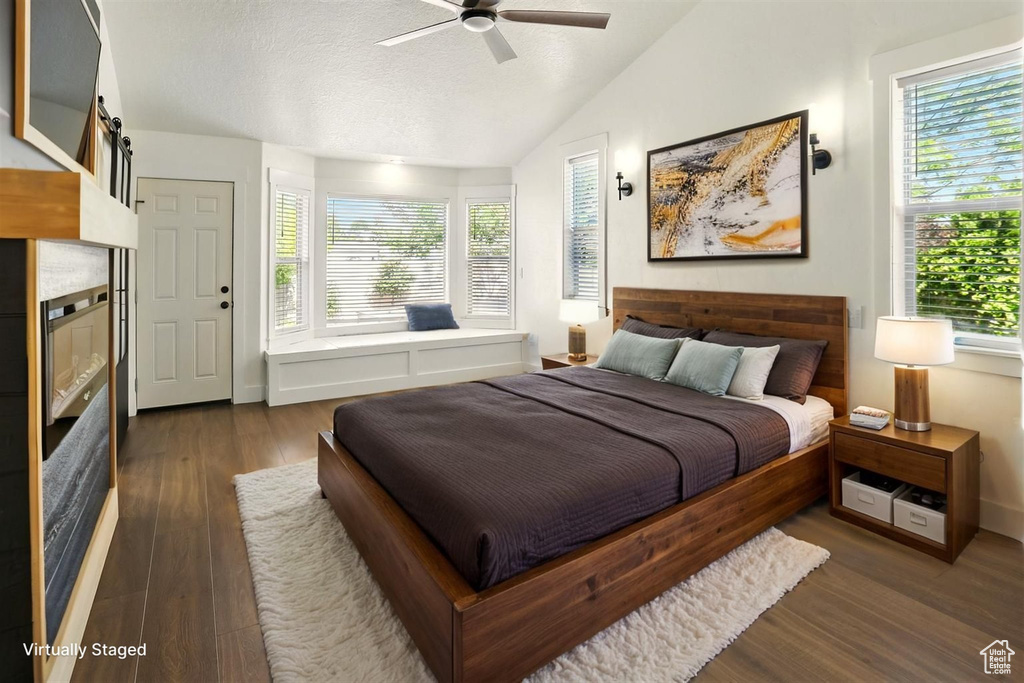 Bedroom featuring multiple windows, vaulted ceiling, dark wood-type flooring, a textured ceiling, and ceiling fan