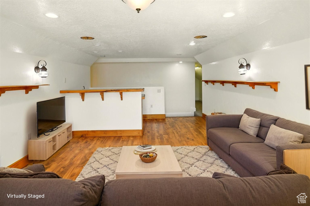 Living area with lofted ceiling, wood finished floors, a textured ceiling, and recessed lighting