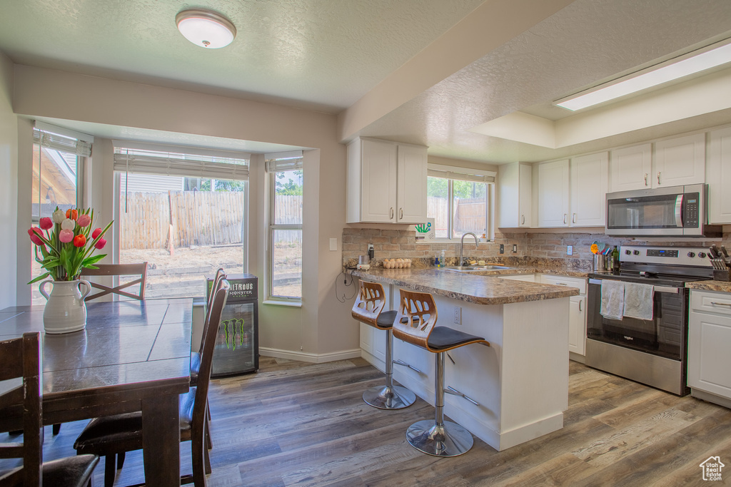 Kitchen with stainless steel appliances, wood finished floors, a peninsula, white cabinets, and a textured ceiling