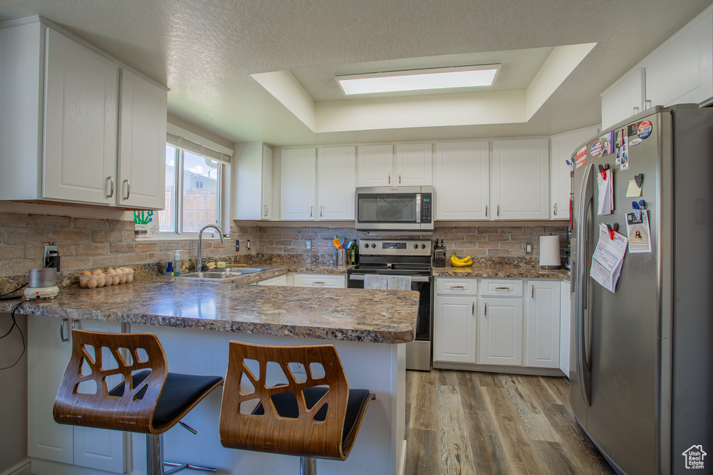 Kitchen with appliances with stainless steel finishes, a peninsula, light wood-type flooring, white cabinets, and tasteful backsplash