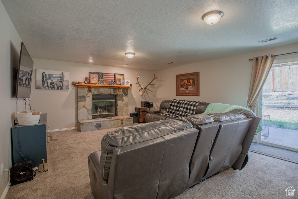 Living room featuring carpet flooring, a textured ceiling, and a stone fireplace