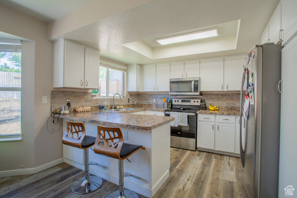 Kitchen featuring stainless steel appliances, a peninsula, light wood-style floors, and tasteful backsplash