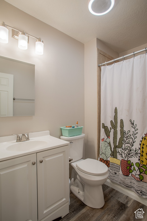 Full bathroom with wood finished floors, vanity, curtained shower, and a textured ceiling