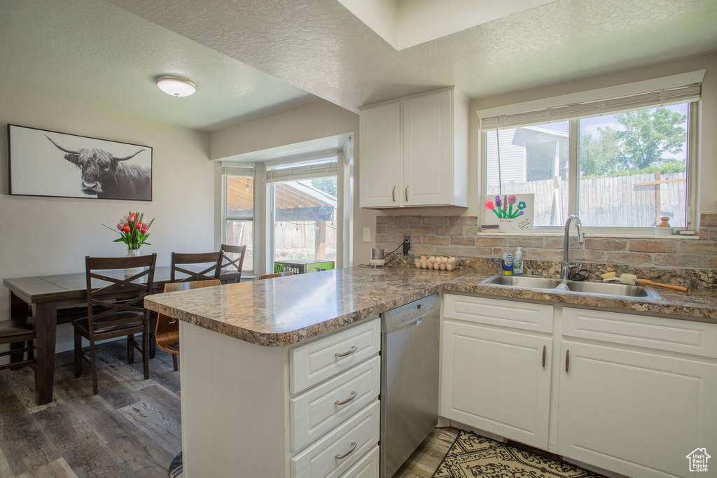 Kitchen with stainless steel dishwasher, wood finished floors, a peninsula, tasteful backsplash, and a textured ceiling