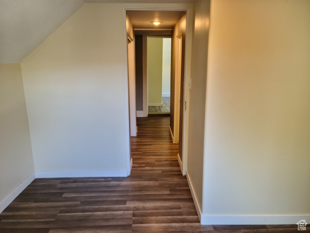 Hall with dark wood-style floors, baseboards, and lofted ceiling