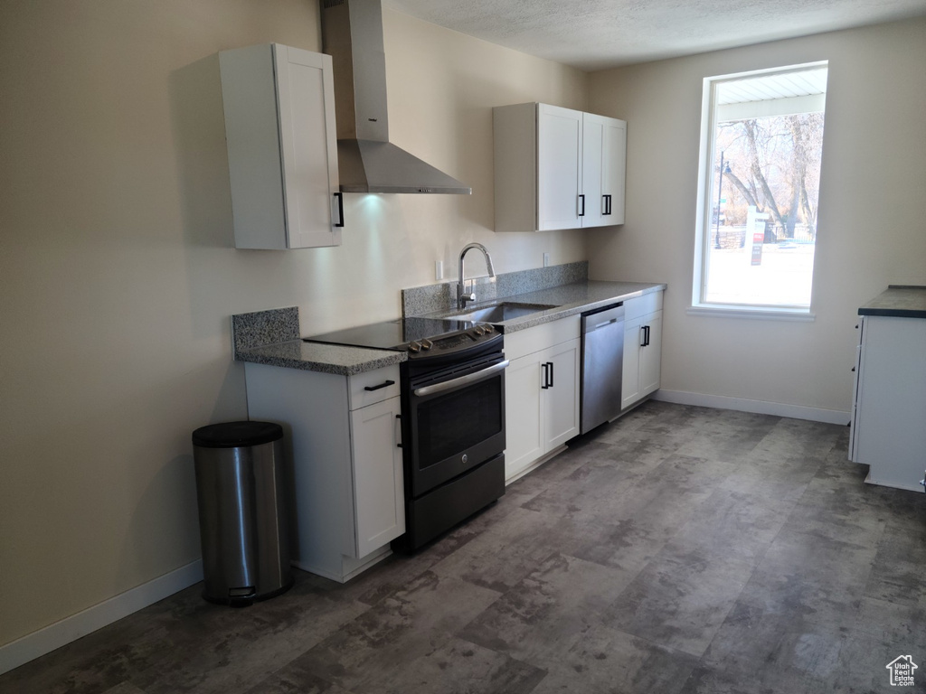 Kitchen featuring wall chimney range hood, electric range, stainless steel dishwasher, a sink, and white cabinets